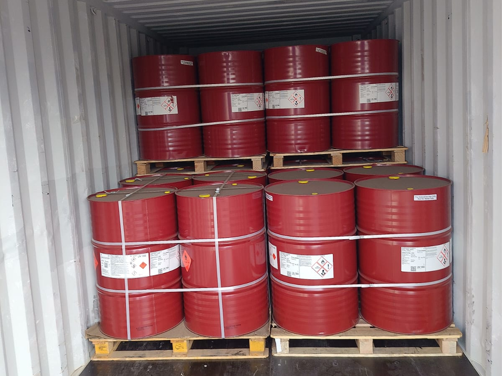 Palletized red industrial chemical drums secured with strapping inside a shipping container for transport.
